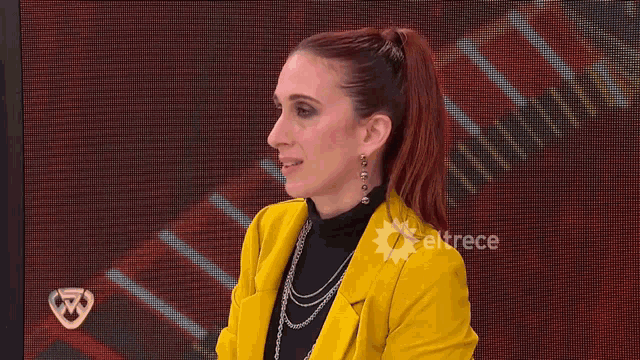 a woman in a yellow jacket is clapping her hands in front of a screen that says eltrece on it