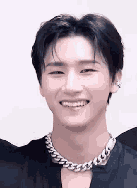 a close up of a young man wearing a chain necklace and smiling .