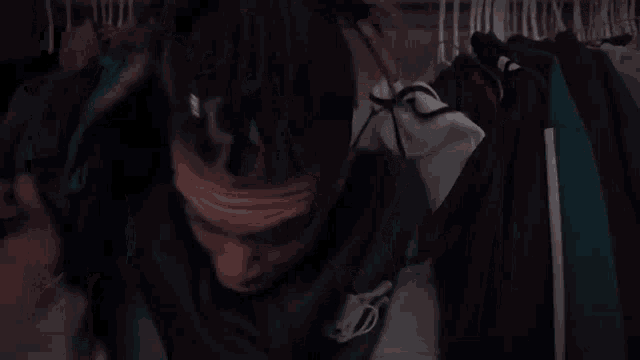 a man with dreadlocks is standing in a closet with clothes hanging on the wall .