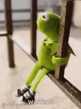 kermit the frog is sitting on a railing and hugging a pole .