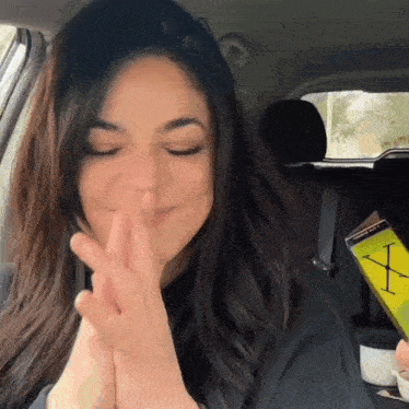 a woman is sitting in a car with her eyes closed and holding a book that says x.