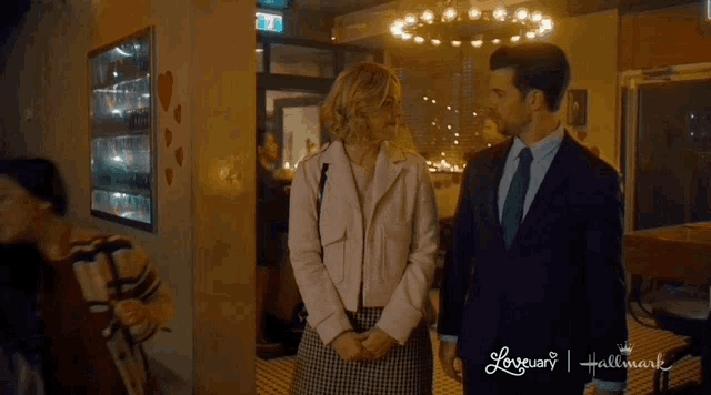 a man and a woman are standing next to each other in front of a hallmark sign