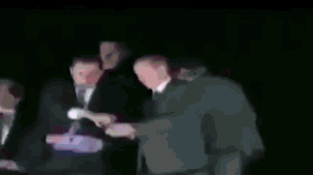a group of men are standing around a man in a suit holding a sign .