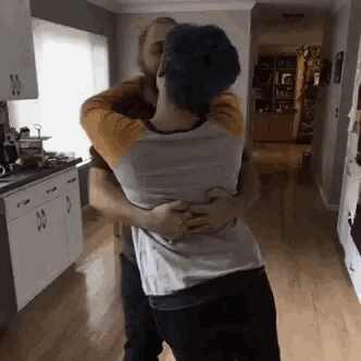 two men are hugging each other in a kitchen in a living room .