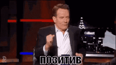 a man in a suit is sitting on a stage with his fist in the air and says positive in russian .
