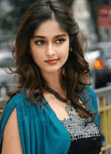 a beautiful young woman wearing a blue jacket and a black top is standing in front of a fence .