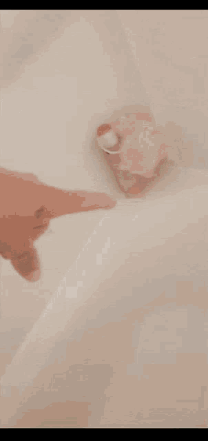 a person 's hand is reaching into a bathtub with a sponge