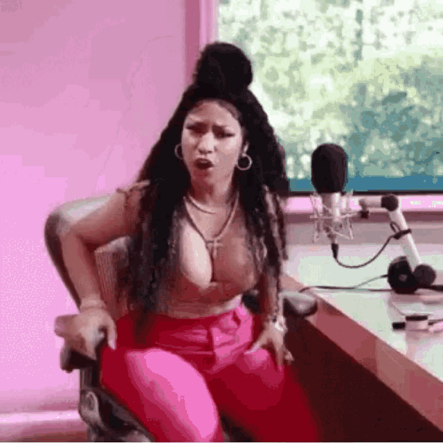a woman in a bra and pink pants is sitting in front of a microphone .