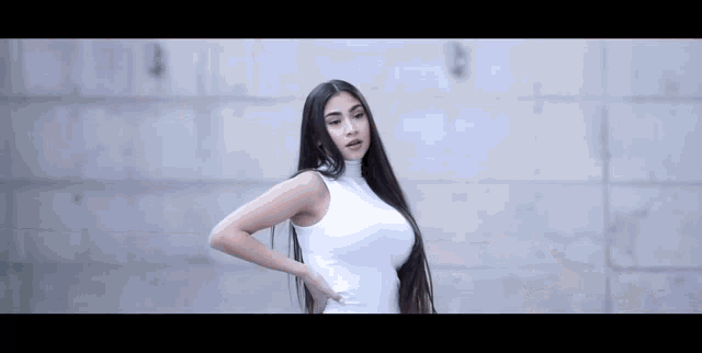 a woman with long hair is wearing a white dress and standing in front of a wall .