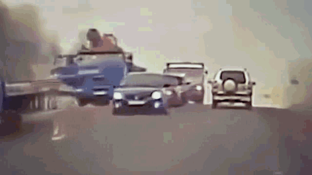 a group of cars are driving down a highway with a person riding on the back of a truck .