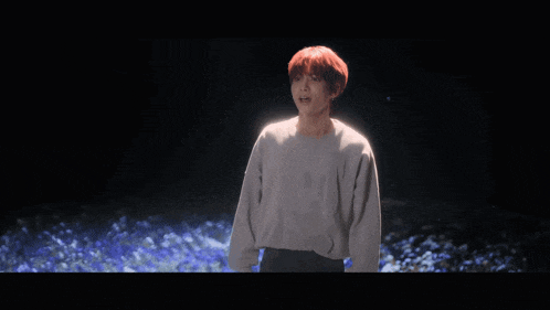 a man with red hair is standing in front of a field of blue flowers
