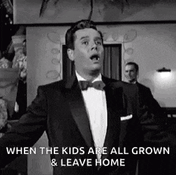 a man in a tuxedo is standing in a room with his arms outstretched in a black and white photo .