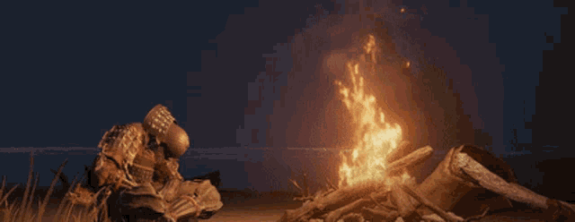 a man sits in front of a fire on the beach at night