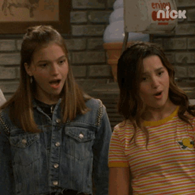 two girls are standing next to each other in front of a sign that says " enjoy nick "