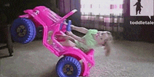a little girl is riding a pink toy car on her back .