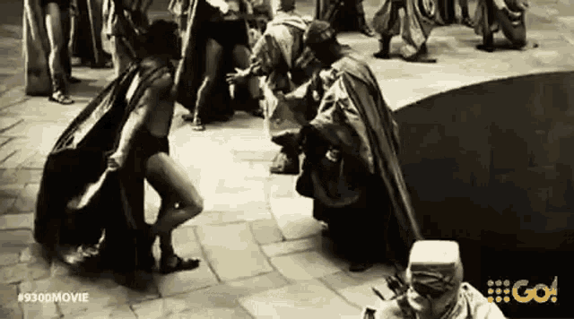 a black and white photo of a group of people standing around a large hole in the ground .