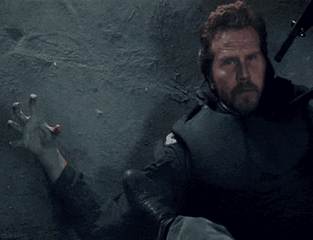 a man with a beard is laying on the ground in a dark room holding a gun .