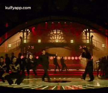 a group of people are dancing on a stage in front of a large crowd .