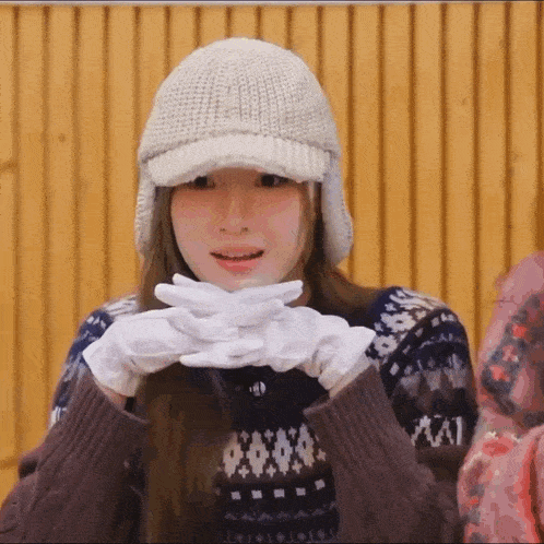 a girl wearing a hat and gloves is making a face