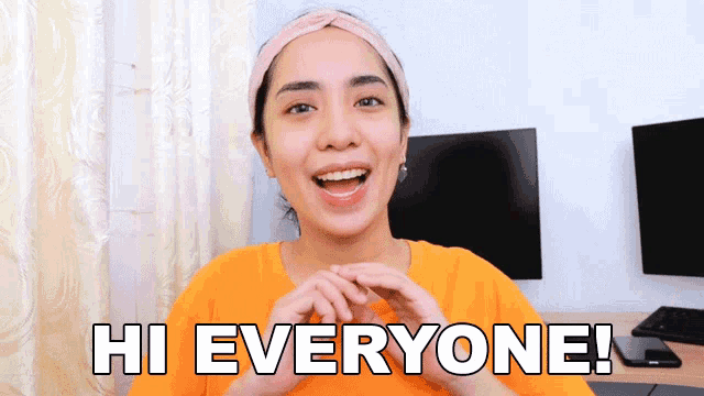 a woman says hi everyone in front of a computer monitor