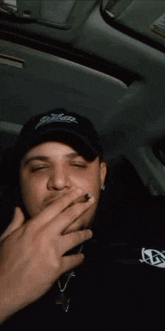 a man is smoking a cigarette in a car while wearing a hat .
