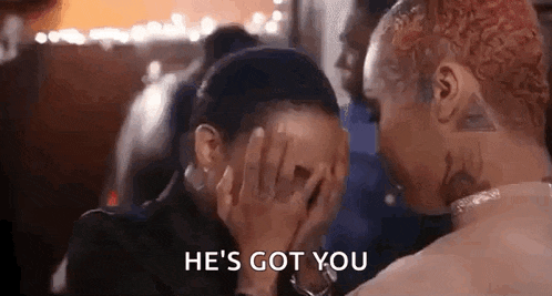 a man and a woman are sitting next to each other and the man is covering the woman 's face with his hands .