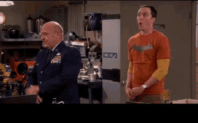 a man in an orange batman shirt stands next to a man in a blue suit