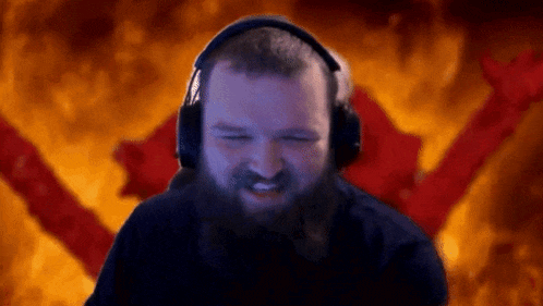 a man with a beard is wearing headphones and making a funny face in front of a fire background .