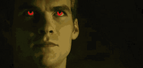 a man with red eyes is looking at the camera in the dark .