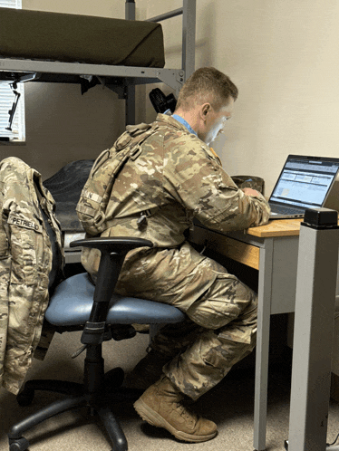 a man in a military uniform is sitting at a desk with a laptop on it
