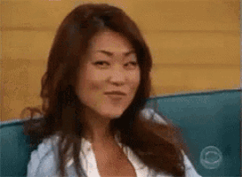 a woman with long brown hair is sitting on a blue couch and making a funny face .