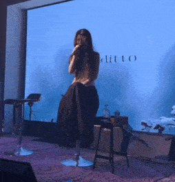 a woman singing into a microphone in front of a wall with the word ditto on it