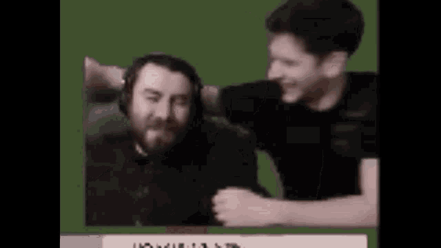 two men are sitting next to each other on a green background and one of them is wearing headphones .