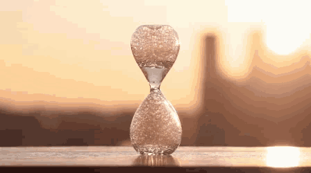 an hourglass is sitting on a wooden table with the sun behind it
