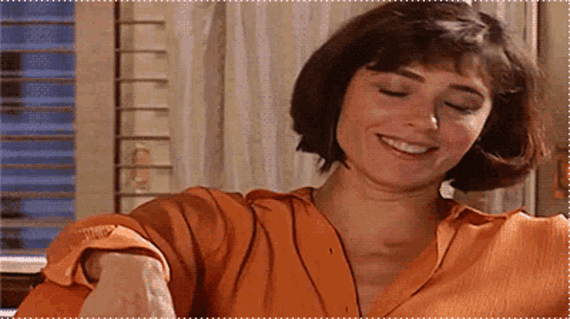 a woman wearing an orange shirt is smiling and looking at the camera