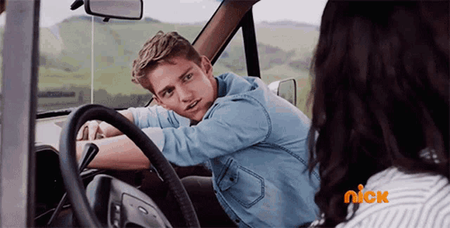 a man leaning on the steering wheel of a car next to a woman with a nick logo on her shirt