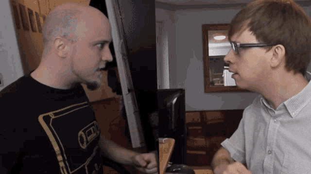 a man wearing a black shirt with a gold circle on it is talking to another man