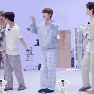 a man in a blue hoodie and plaid pants is dancing in a room with other people