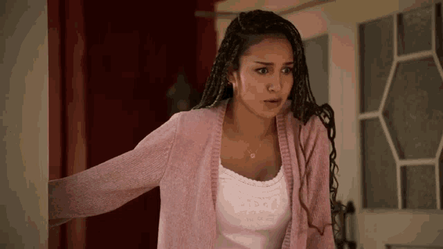 a woman with braids is wearing a pink sweater and a white tank top .