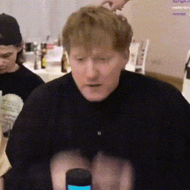 a man in a black shirt is sitting at a table with a microphone in his hand .