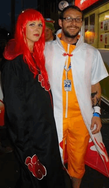 a man and a woman are posing for a picture . the woman has red hair and the man has orange shorts .