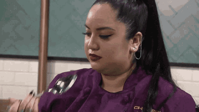 a woman in a purple chef 's jacket is holding a spoon and fork .