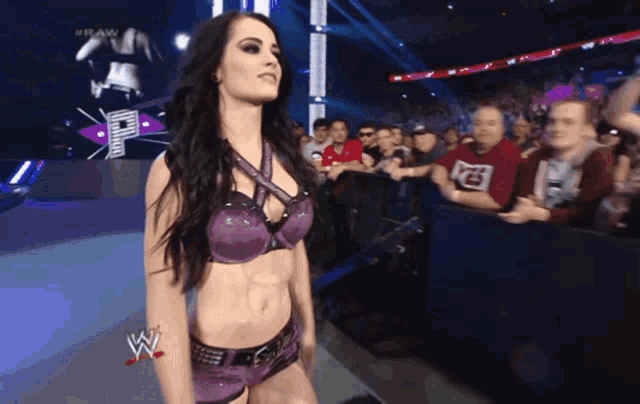 a female wrestler in a purple outfit stands in front of a crowd