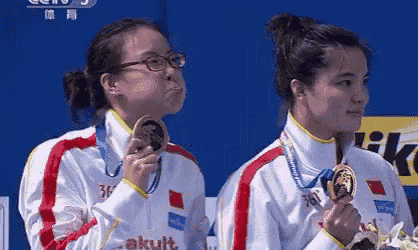 two female athletes are holding up their medals and one is wearing glasses