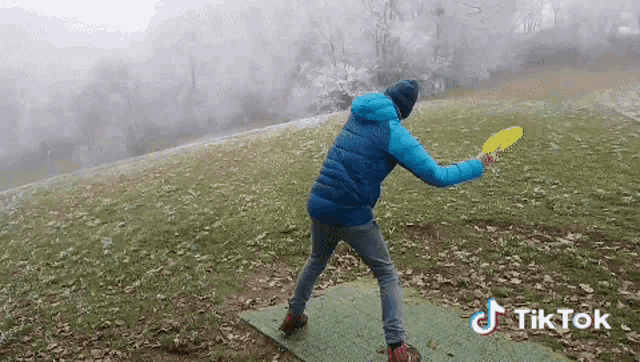 a man in a blue jacket is throwing a frisbee on a green mat with a tiktok watermark