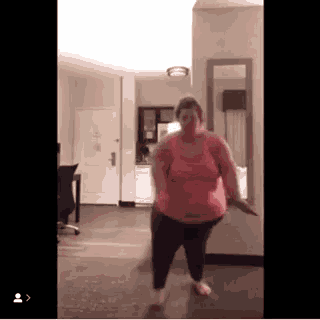 a woman in a pink tank top is dancing in a room in front of a mirror .
