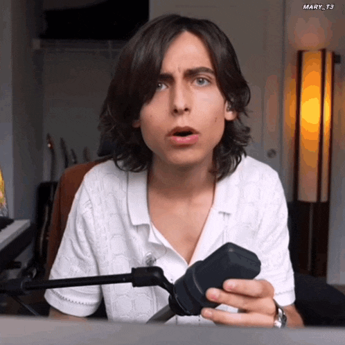 a man with long hair is holding a microphone and making a surprised face .