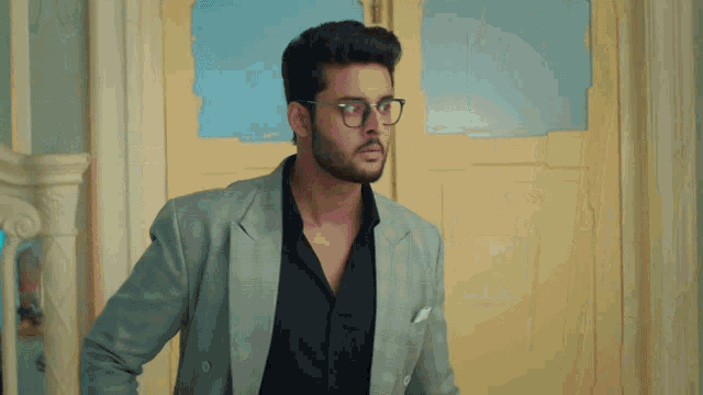 a man wearing glasses and a grey jacket stands in front of a door