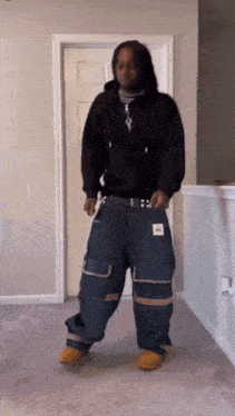 a man in a black hoodie and blue cargo pants is standing in front of a door .