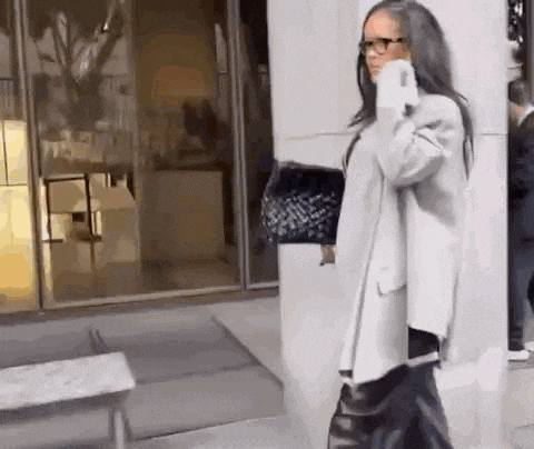 a woman wearing glasses and a gray coat is walking down a street .